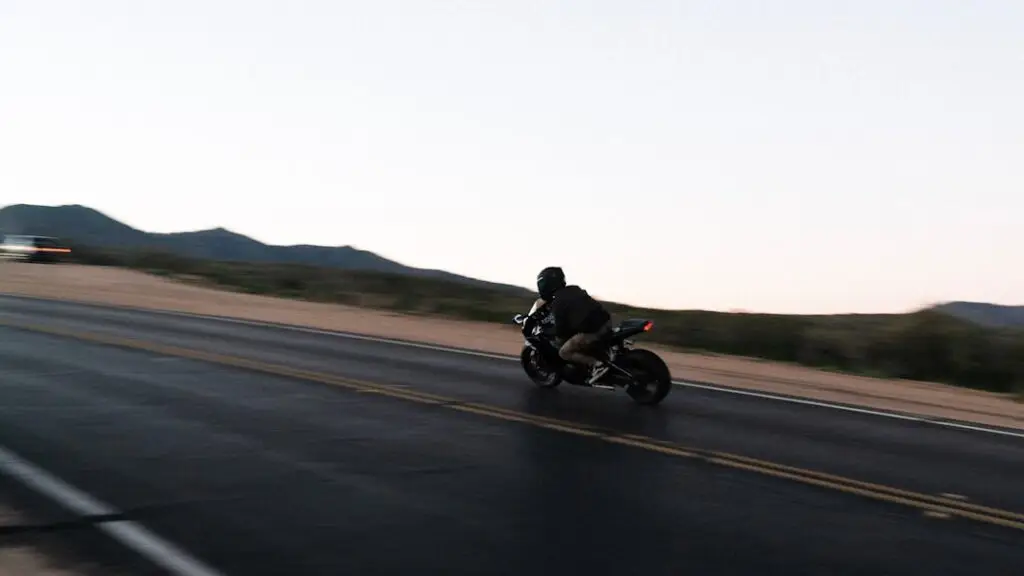 Siyah montlu sürücü gündüz dağ yolunda motosiklet kullanıyor
