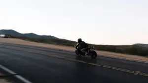 Siyah montlu sürücü gündüz dağ yolunda motosiklet kullanıyor