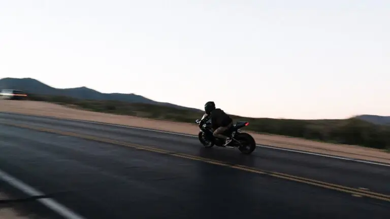 Siyah montlu sürücü gündüz dağ yolunda motosiklet kullanıyor