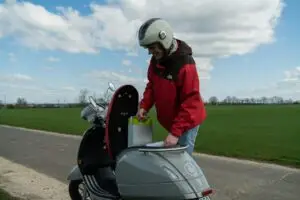 Kırmızı montlu sürücü gündüz elektrikli scooter kullanıyor