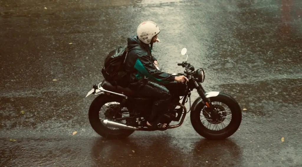 Yağmurdan ıslanmış bir sokakta motosiklet s&uuml;ren s&uuml;r&uuml;c&uuml;