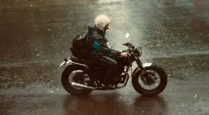 Yağmurdan ıslanmış bir sokakta motosiklet süren sürücü